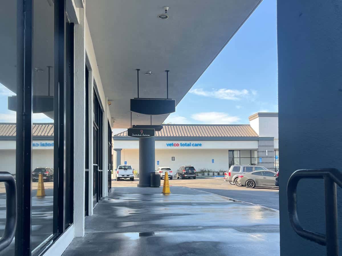 Covered storefront walkway drying after pressure washing, with the parking lot and neighboring shops beyond