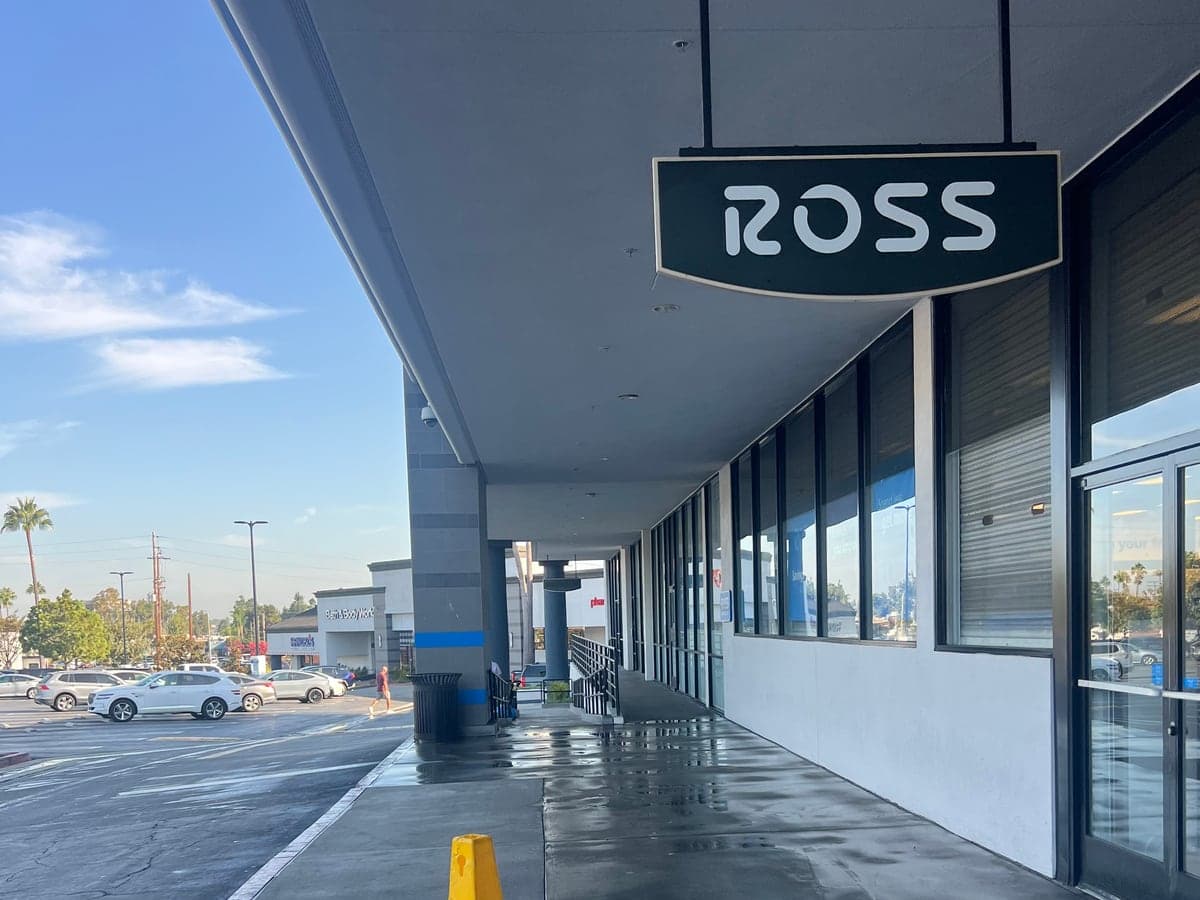 Storefront sidewalk under a department-store sign, freshly pressure washed with a wet-floor cone