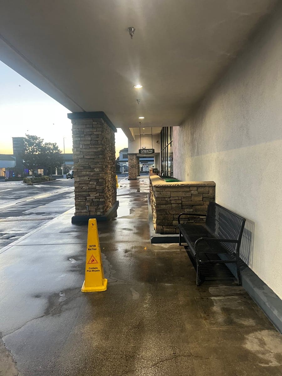 The same covered retail walkway after pressure washing, concrete clean and still wet with a caution cone in place